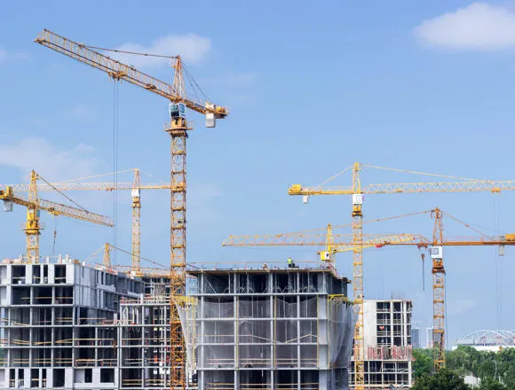Buildings under construction with cranes and workers on the site.